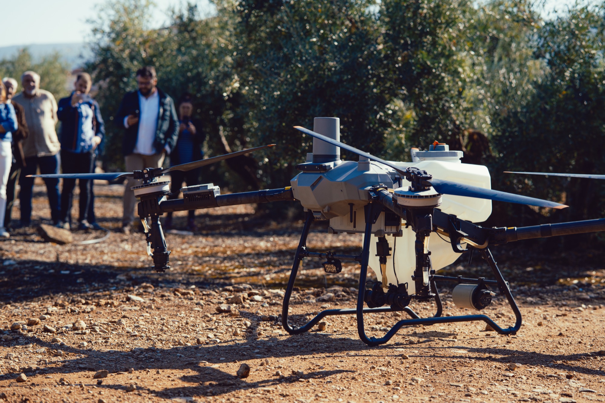 Dron agrícola con personas al fondo durante una visita al olivar